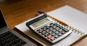 Calculadora e caderno ao lado de um notebook sobre a mesa